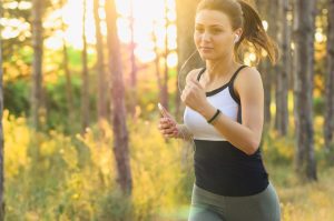 Image shows a woman taking exercise by running in the woods with headphones and a portable media player.