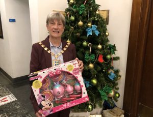 Mayor of Sefton holding a oy in front of a Christmas tree