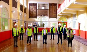 Photograph of Sefton councillors, MP, project contractor and Council officers wearing hard hats and PPE in the Centre's main hall.