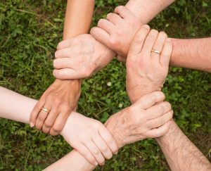 Image shoes hands and forearms of six people interlocked and supporting each other