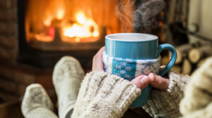 Image of someone staying warm next to a fire while holding a hot drink