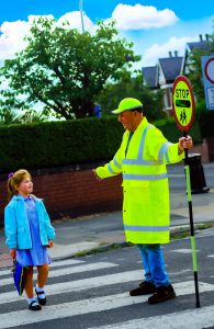 School crossing patrol helping child to cross the road