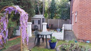 A patio area in a care home with low walls surrounding and flowers covering an archway leading in.