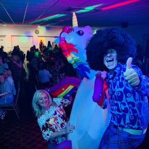 A room with disco lights, an inflatable unicorn and two people in costume smiling at the camera