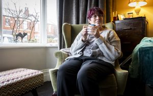 Person in their living room, looking happy and holding a mug.