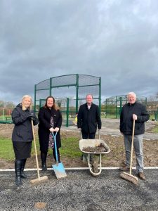 Councillors holding tools such as a wheelbarrow and shovel.